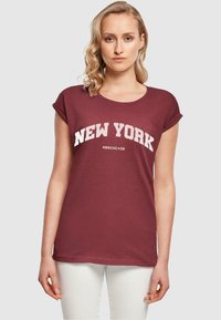 Maroon t-paita, jossa on käännetyt hihat, ja jossa on valkoiset tekstit "NEW YORK" ja "MERCHCODE" pehmeässä kankaassa. Yksinkertainen, rento muotoilu.