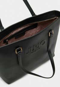 Czarna torba typu tote wykonana ze sztucznej skóry z wytłoczonym logo, zamknięciem na górny zamek błyskawiczny oraz wewnętrzną wyściółką w wzory. Posiada dwa paski na ramiona.