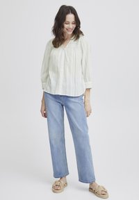 Camicia button-up a righe leggere con scollatura a V, maniche a tre quarti, abbinata a jeans a gamba dritta e lavaggio chiaro e sandali intrecciati.