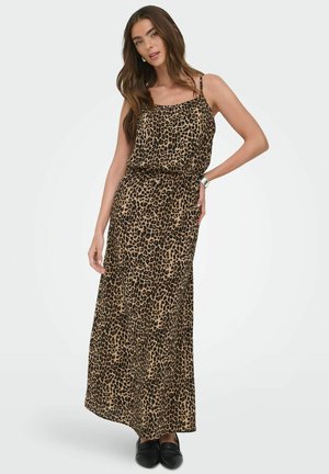 Kvinde iført en ærmeløs maxikjole med leopardprint kombineret med sorte flade sko, poserer med den ene hånd på hoften og løst hår.