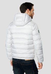 Hvid dunjakke med hætte, der har vandret quiltning, elastiske manchetter og et logo-patch på venstre skulder.