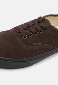 Brauner Wildleder-Sneaker mit abgerundeter Spitze, schwarzer Gummisohle und strukturierten Schnürsenkeln. Verfügt über ein dezentes Markenlogo an der Seite.