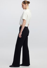Witte cropped top met korte mouwen en een ritsdetail op de rug, gecombineerd met zwarte high-waisted broek met wijde pijpen. Soepele textuur en perfect pasvorm.