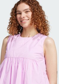 Ljusrosa ärmlös klänning med rund halsringning, rynkad midja och mjuk textur. Har subtil branding på framsidan.