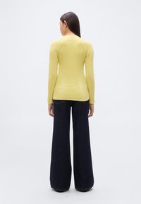 Κίτρινη μπλούζα με μακριά μανίκια και ριγέ υφή, με εφαρμοστή σιλουέτα, συνδυασμένη με σκούρα μπλε τζιν παντελόνι με φαρδιά μπατζάκια. Λείο ύφασμα, μινιμαλιστικός σχεδιασμός.