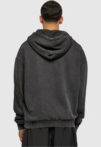 Haut à capuche gris foncé avec une coupe décontractée, doté d'une grande capuche confortable et de poignets et d'un ourlet côtelés. Tissu texturé avec une apparence douce.