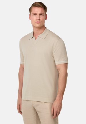Polo shirt beige a maniche corte con colletto, caratterizzato da una texture liscia e sottili dettagli bianchi sulle maniche.