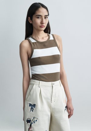 Canotta a coste a righe marroni e bianche con scollo tondo. Abbinata a pantaloni larghi color crema ricamati con motivi floreali.