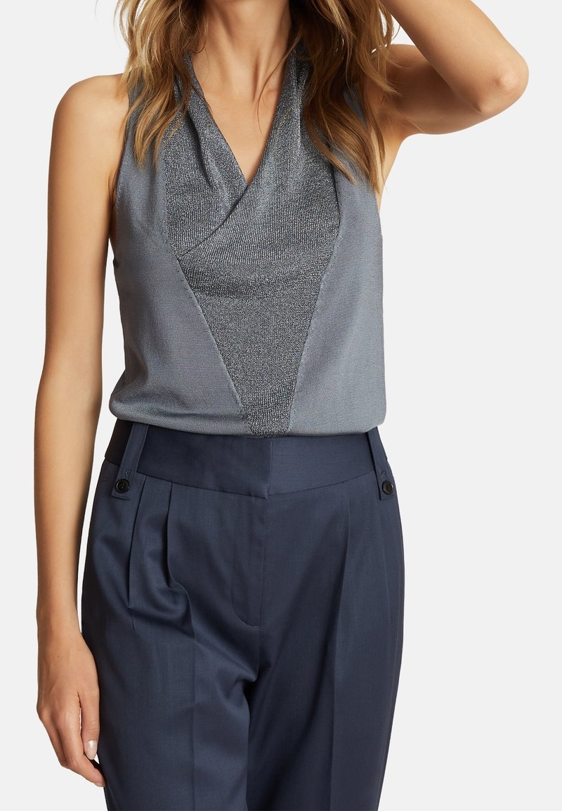Haut à col halter gris avec un accent métallique texturé au centre, associé à un pantalon noir marine tailleur avec des plis et un détail en bouton.
