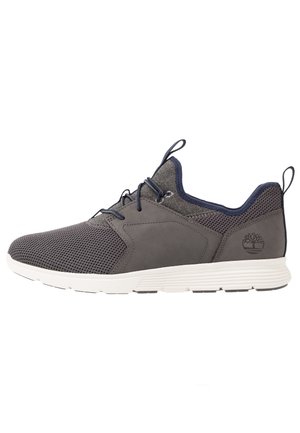 Baskets gris foncé avec partie avant en mesh, lacets foncés, semelle blanche coussinée et languettes de traction sur la languette et le talon, vue de profil sur fond blanc.