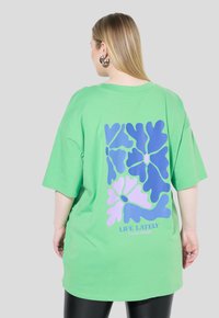 Zelené oversized tričko s květinovým potiskem v modré a růžové barvě na zádech, se sloganem "LIFE LATELY" na spodním okraji. Krátké rukávy.