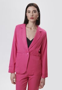 Blazer rosa con chiusura a un solo bottone, revers a punta, tasche frontali e maniche lunghe; tessuto liscio e su misura.