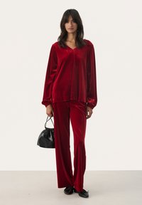 Red velvet loungewear set featuring a loose-fitting top with a V-neck and long sleeves, paired with wide-leg pants; includes a black handbag.