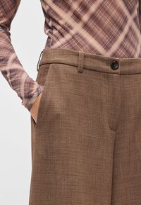 Καφέ παντελόνια από υφασμάτινη υφή, με σχεδιασμό ευθείας γραμμής, θηλιές για ζώνη και κλείσιμο με ένα κουμπί.