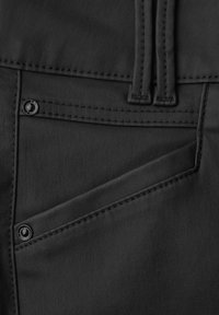Tela negra con una textura suave, que presenta un bolsillo diagonal, costuras en contraste y un detalle de botón de metal negro.