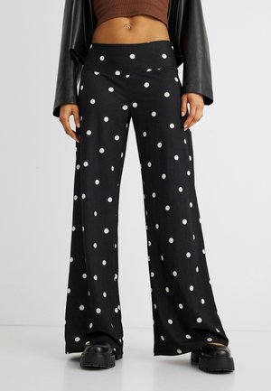 Person som har på seg svarte vide bukser med hvite polkaprikker, en kort brun topp, en svart skinnjakke og tykke svarte sko.