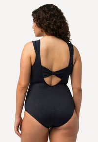 Maillot de bain noir avec un dos décolleté et un détail de nœud. Fabriqué à partir d'un matériau lisse avec un motif léopard subtil. Bretelles ajustables pour un ajustement parfait.