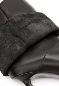 Tacchi alti in pelle nera con una morbida fascia in suede nero davanti; design elegante con punta appuntita e finitura lucida.