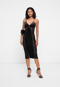 Μαύρο midi φόρεμα με πλαϊνές λαβές από δαντέλα, λεπτές τιράντες, εφαρμοστή σιλουέτα και V-λαιμό. Συνδυασμένο με μαύρες ψηλές γόβες.