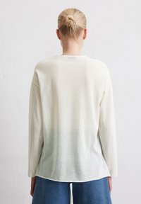 Langärmliges Rundhalsshirt in Off-White, mit einer leicht durchscheinenden Textur und einem Farbverlaufssaum zu einem sanften Blau. Lockere Passform, minimales Branding.