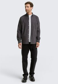 Camisa de manga larga, con botones, en algodón gris oscuro, con un bolsillo en el pecho, combinada con jeans negros y zapatos negros. Diseño simple y estructurado.