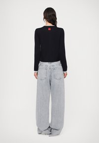 Μαύρο μπλουζάκι με μακριά �μανίκια και κόκκινη ετικέτα, συνδυασμένο με ανοιχτό γκρι παντελόνι με φαρδιά πόδια, που δείχνει άνετη εφαρμογή και τυπικό σχέδιο πίσω τσέπης.