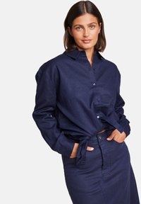 Mørkeblå lin skjorte med krage, knappelukking foran og lange ermer. Kombinert med en matchende tykk skjørt med knappelukking og lommer.