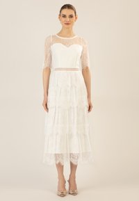 Witte kanten jurk met een gelaagde rok, korte kanten mouwen, een sweetheart-uitholling en een decoratieve riem met een horizontaal uitsnijdetail.