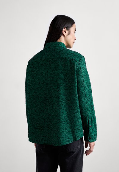 Veste verte texturée avec un motif chevrons, dotée d'un col classique, de poignets à boutons et d'une coupe décontractée, vue de dos.