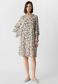 Sukienka o krótkich rękawach, sięgająca do kolan, w beżowym kolorze z czarnym nadrukiem węża; posiada falbaniaste rękawy i wiązanie przy dekolcie. Miękki materiał.