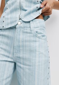 Top in denim blu chiaro a righe con chiusura a zip e bottoni a pressione, abbinato a pantaloni in denim blu chiaro con bottoni laterali e tasche.