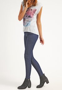 Gray short-sleeve t-shirt with graphic design, paired with dark blue skinny jeans and black ankle boots featuring a side zipper.