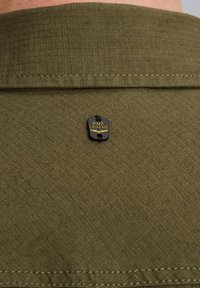 Camicia verde oliva in tessuto testurizzato, con un'etichetta nera che recita "PME LEGEND" attaccata vicino al colletto. Dettagli di cuciture doppie.