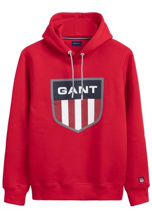 Rød hættetrøje med frontskjoldlogo med teksten "GANT" over røde og hvide lodrette striber og snore i hætten.