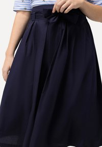 Navy midi-jurk gemaakt van lichtgewicht stof. Kenmerkt zich door een aansluitende taille met een strikdetail en plooien voor volume. Soepele textuur.