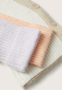 Tre strikkede stofprøver: lavendel, fersken og creme. Hver har en blød tekstur med et ribbet mønster og færdiggjorte kanter. En beige knap som detalje er synlig.