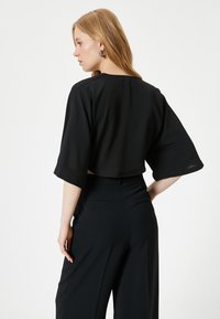 Sort cropped bluse med brede ærmer; letvægtsstof; glat tekstur. Sammen med højhalset sorte bukser; minimalistisk design.