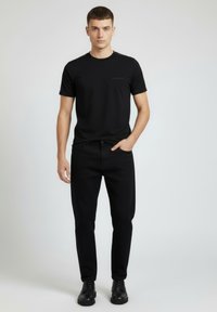 Czarny t-shirt z okrągłym dekoltem i krótkimi rękawami z delikatnym logo. Do tego czarne jeansy o prostych nogawkach oraz czarne sznurowane buty.