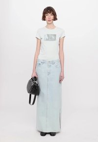 Hele sinine denim maxi seelik, millel on ees lõhik, koos ülikitsa heledat halli T-särgiga, millel on graafiline kujundus, ja must käekott.