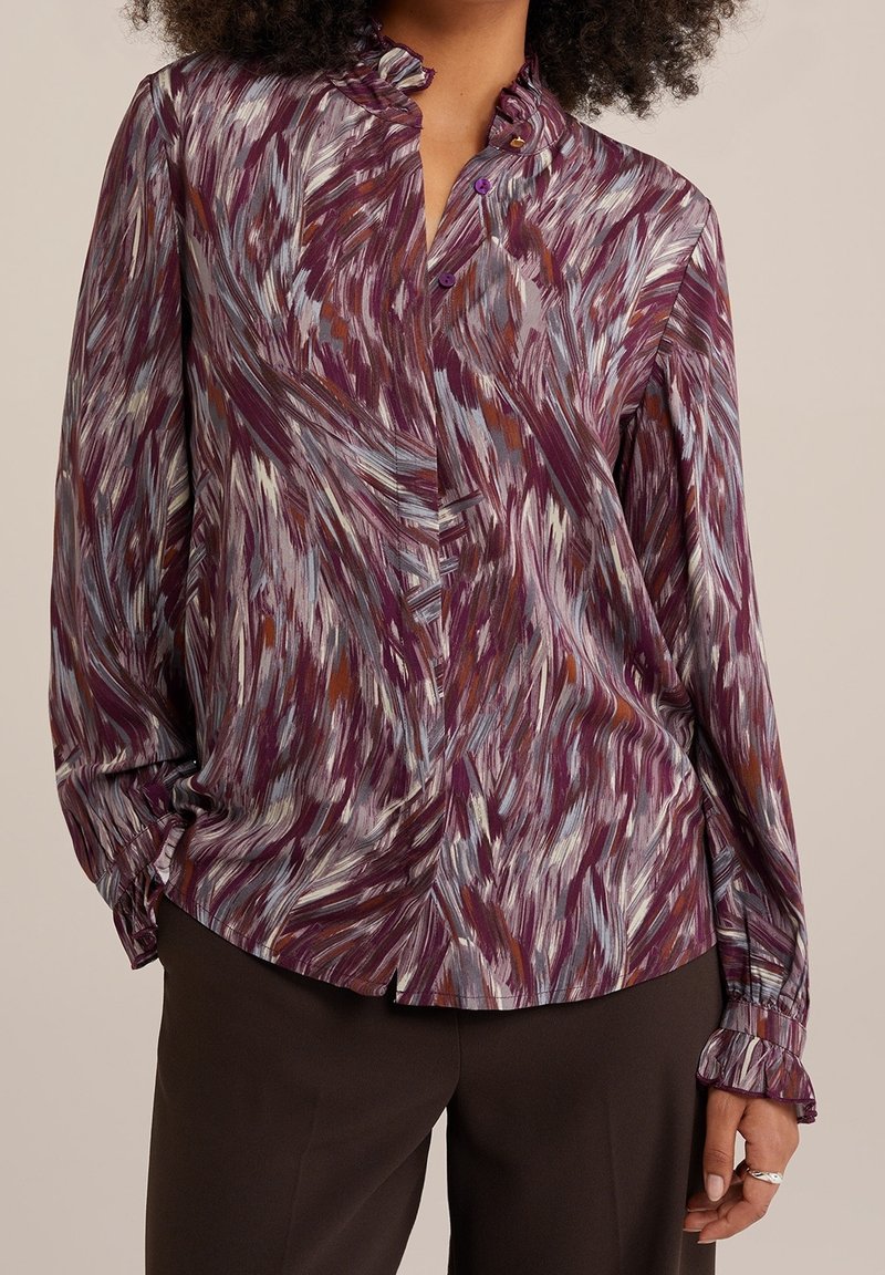 Long-sleeve blouse in a multicolored abstract pattern of purple, gray, and muted orange; features a ruffled collar and button closure.