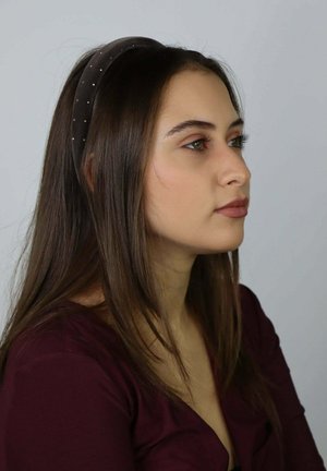 Brązowa aksamitna opaska z małymi srebrnymi koralikami, gładka w dotyku, zaczesujące ciemne włosy do tyłu, modelka w bordowym topie, widok z profilu.