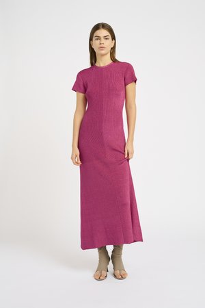 Fitted, short-sleeve maxi dress in textured magenta fabric with a straight silhouette, and side slit, worn with beige heeled sandals.