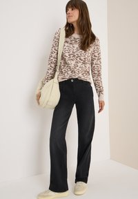 Pull en imprimé léopard beige, pantalons larges noirs, sac à épaule crème et baskets claires. Tissu lisse avec des détails de couture visibles.
