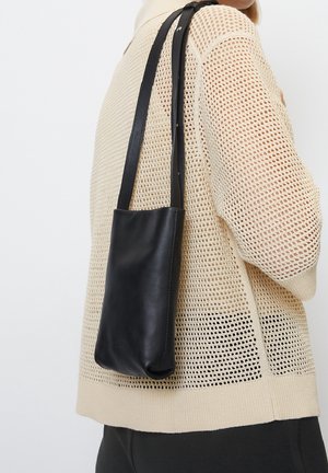 Czarna skórzana torba na ramię o prostym, prostokątnym kształcie. Pasek jest smukły i regulowany, co współgra z fakturowanym, otwartym swetrem.