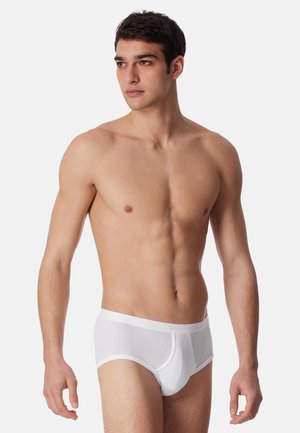Witte katoenen slips met een zachte tailleband, voorzien van een gevormde pouch, een gladde textuur en een aansluitend ontwerp. Model getoond met blote bovenlichaam.