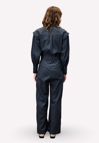 Combinaison rayée sombre avec col, manches longues et taille cintrée. Le tissu est texturé et le pantalon est évasé. Vue de dos présentée.