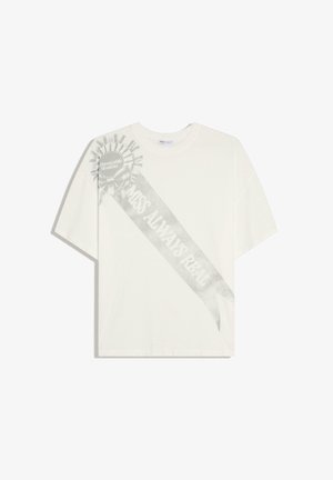 Tricou alb cu mâneci scurte, cu un grafic de panglică gri estompată pe care scrie „Miss Always Real” și o cocardă etichetată „Mențiune Onorabilă” pe umărul stâng.