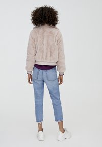 Fuzzy beige bomberjakke med ribbede manchetter, parret med mid-rise lyseblå jeans. Hvide sneakers med teksturerede accenter fuldender outfittet.
