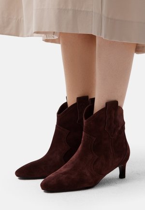 Braune Wildleder-Ankle Boots mit spitzen Zehen und flachen Absätzen, die dekorative gewellter Akzente an den Seiten und eine glatte Textur aufweisen.