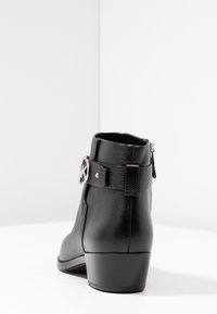Schwarze Leder-Stiefelette mit strukturierter Oberfläche, silbernem Schnallen-Detail und einem flachen Absatz. Verfügt über einen seitlichen Reißverschluss für leichtes An- und Ausziehen.
